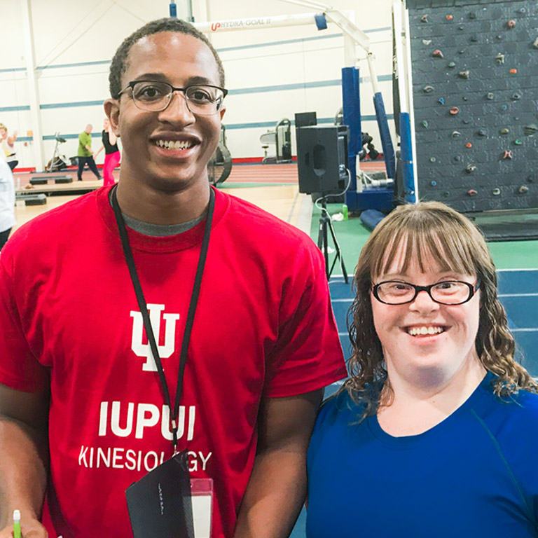 A male AMP instructor in a bright red IUPUI t-shirt poses for a photo with an adult AMP client.