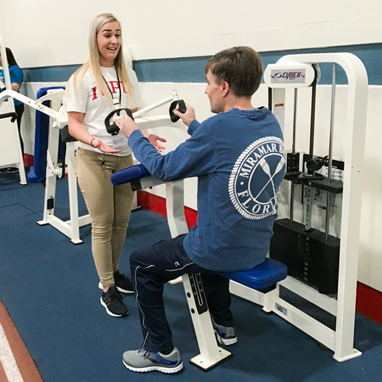 An AMP instructor guides an adult student through use of a triceps fitness machine. 