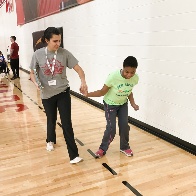 A female instructor helps a school-aged student walk in a straight line in the IUPUI gym.