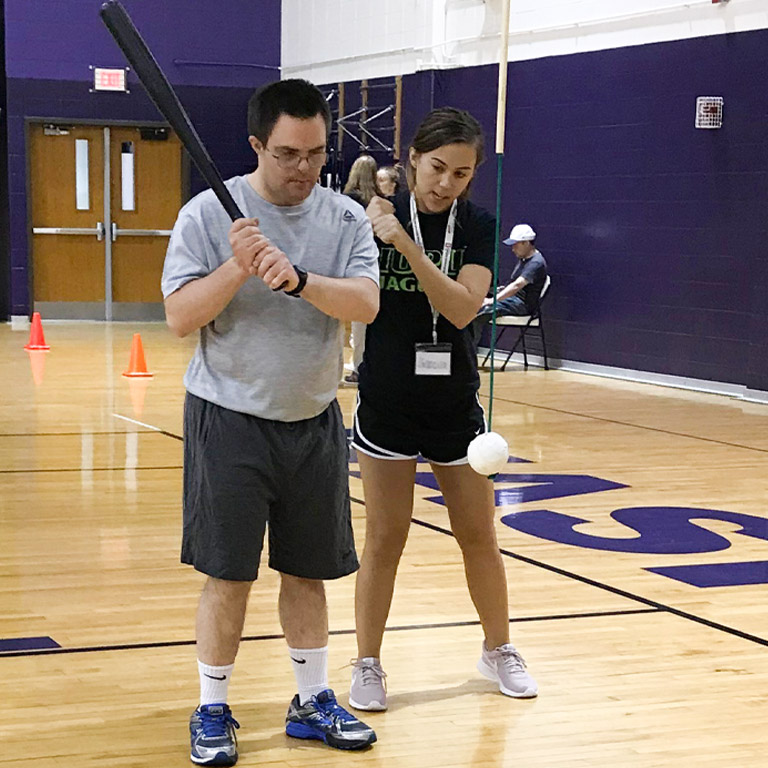 A female AMP instructor demonstrates proper form to an AMP client playing softball.